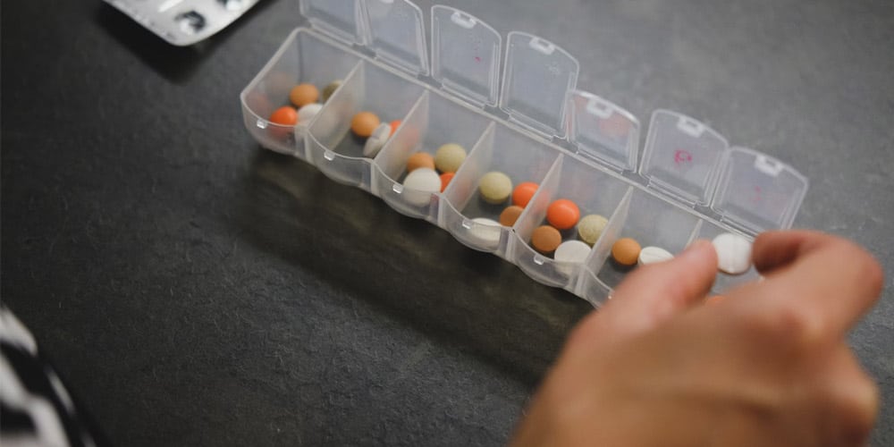 person about to pick medicine from medicine organizer