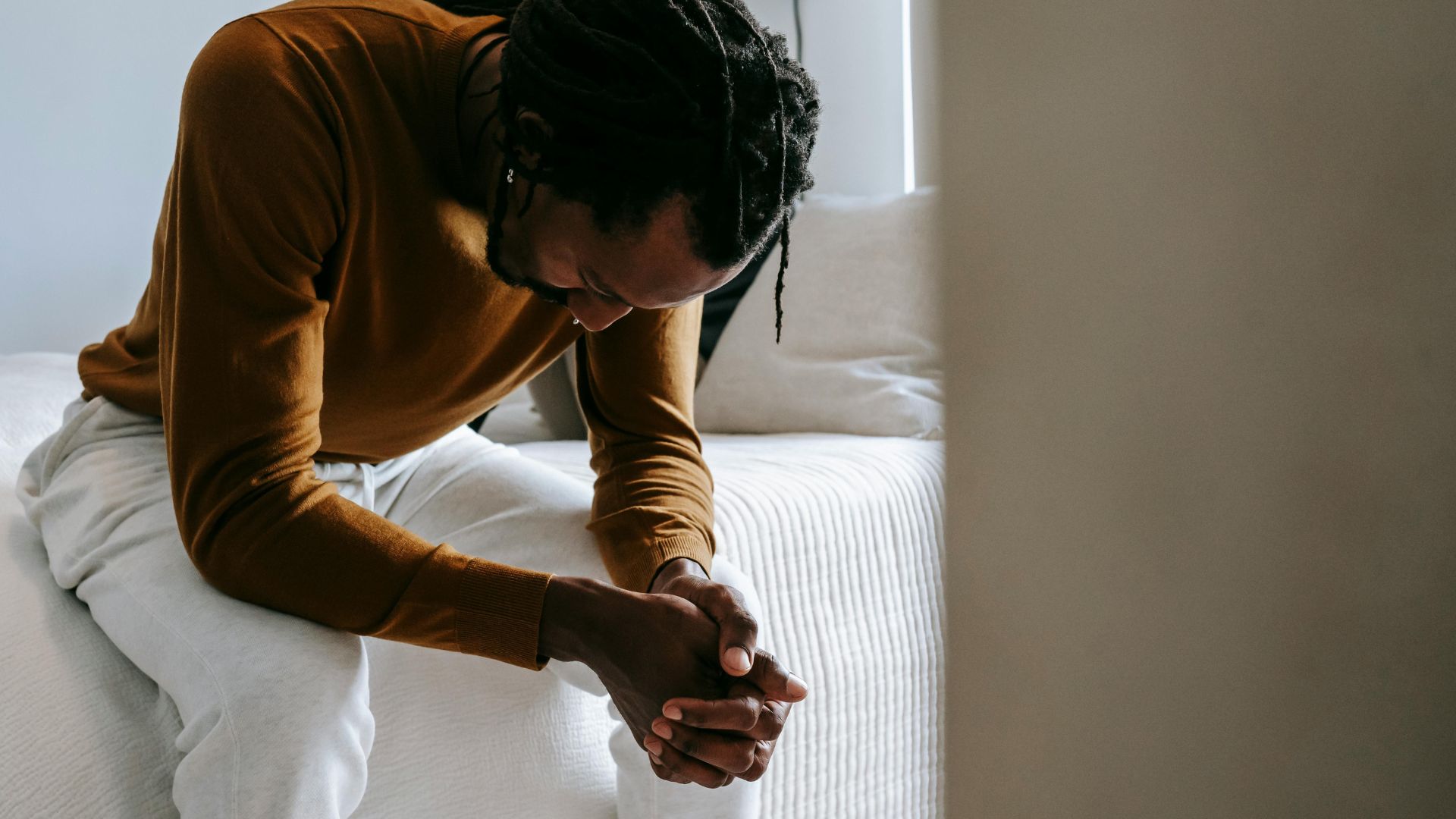 Desperate black man sitting on bed in deep thoughts
