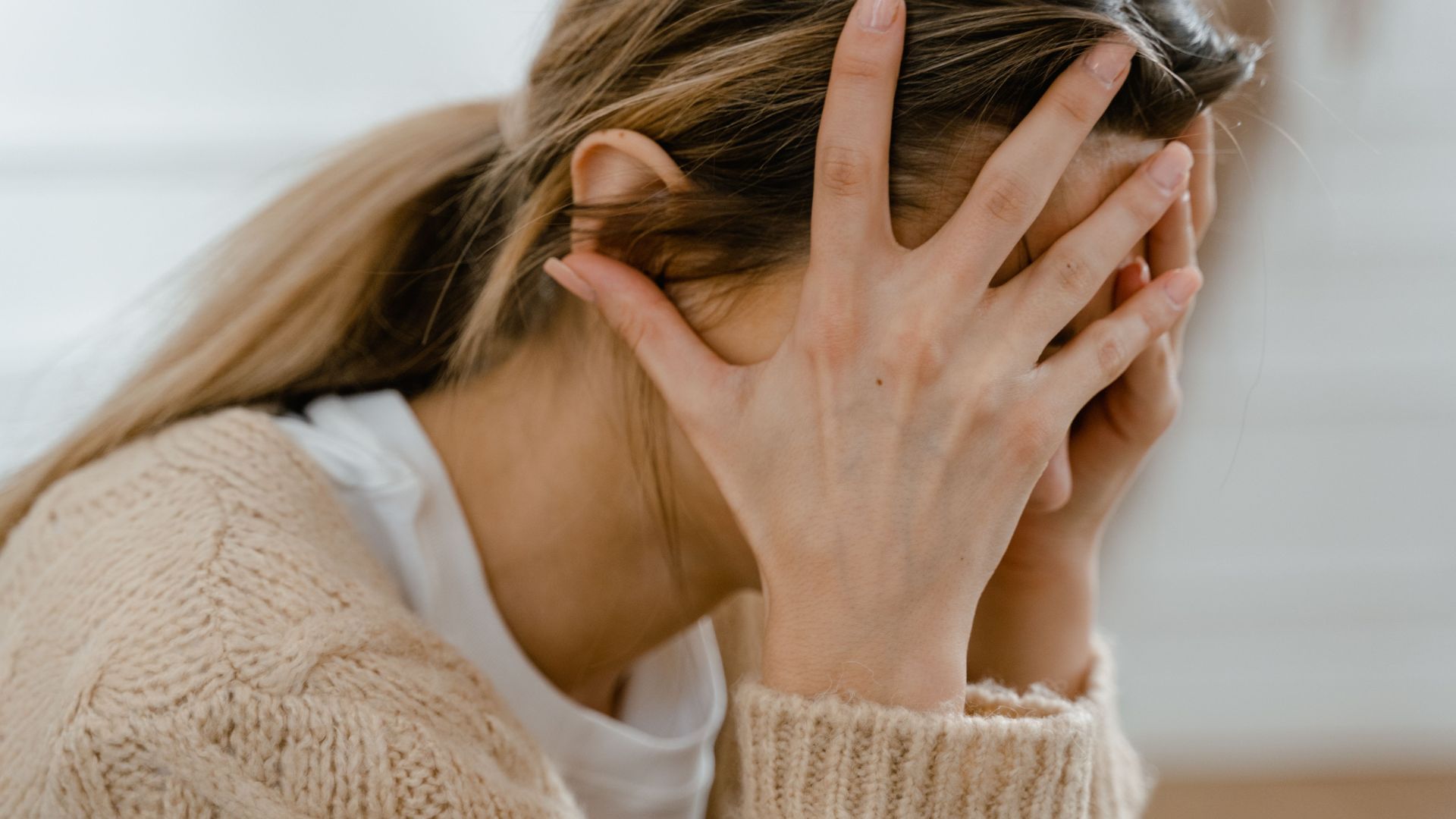 Woman sitting indoors with face covered by hands