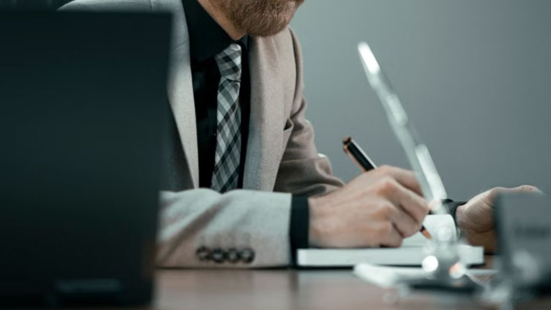 Businessman writing at desk with laptop